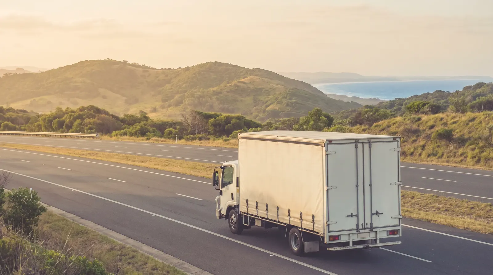 A removal truck heading up the M1 motorway toward the Central Coast, the coastline and a headland in the warm afternoon distance